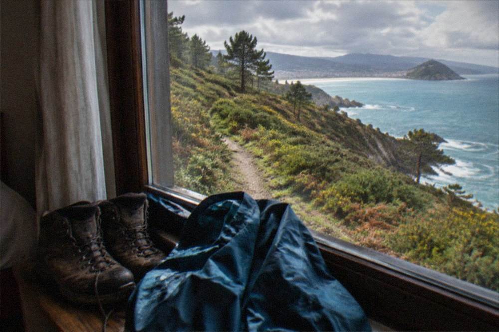 Hiking boots and a rain jacket drying beside a window in a simple guesthouse room