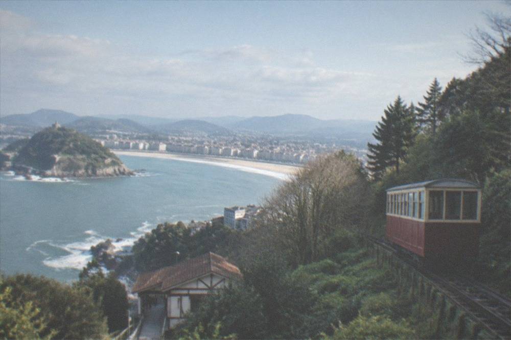 A vintage wooden funicular car climbing a wooded hillside above the bay