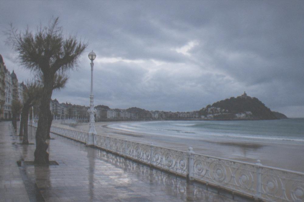 Rain clouds passing over La Concha bay with wet sand and an empty promenade
