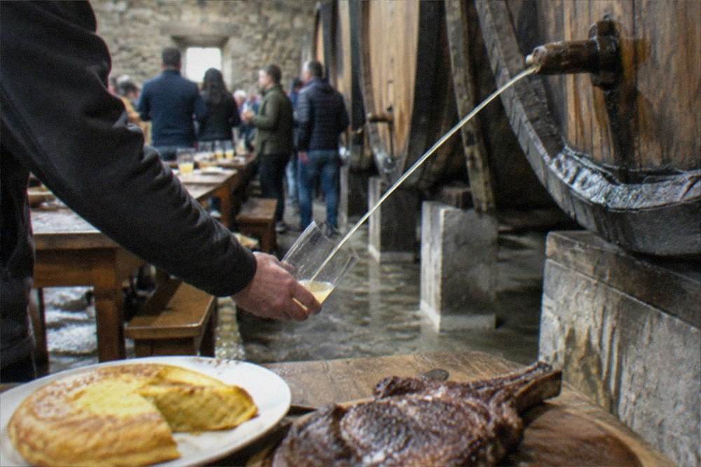 A group of people standing around an open cider barrel in a cellar