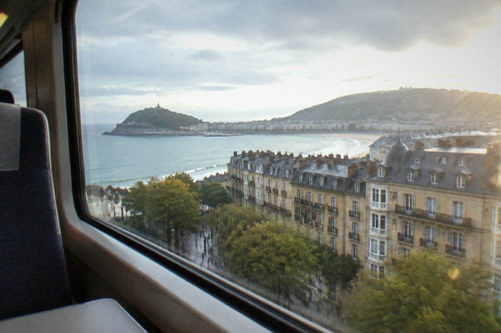 A train interior with clean seats and wide windows looking out toward the Basque coastline