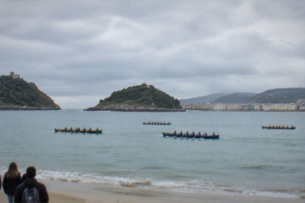 Traditional rowing boats racing across La Concha bay watched from the sand