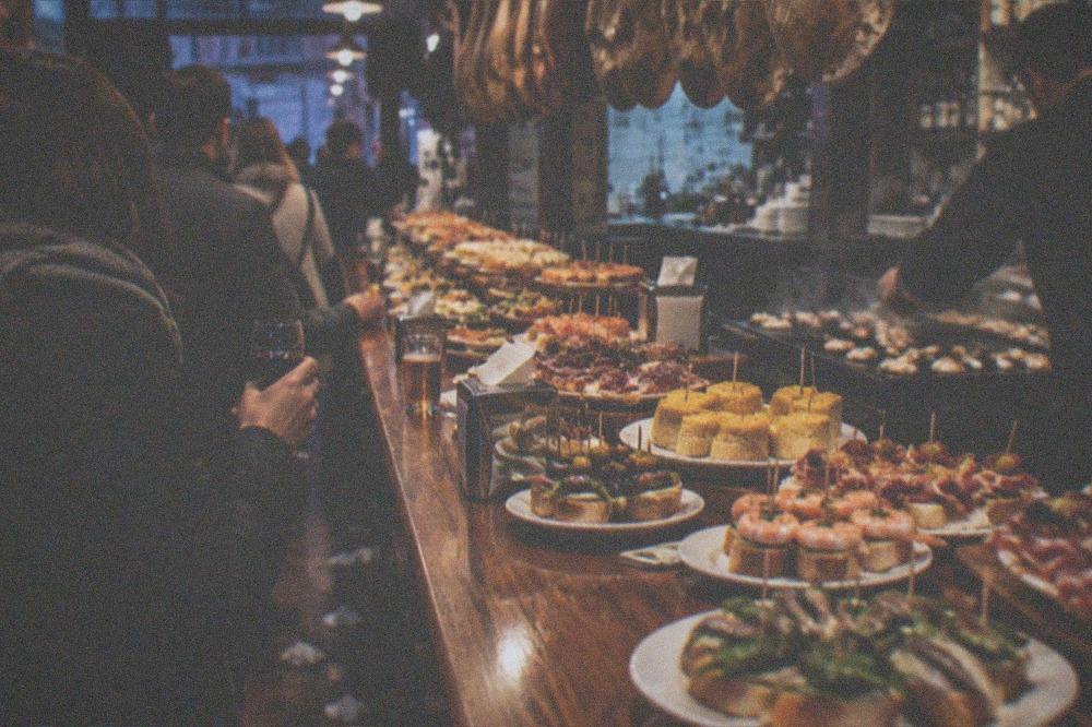 An evening pintxo route in San Sebastián, a bar counter with hot plancha pintxos being served beside skewers