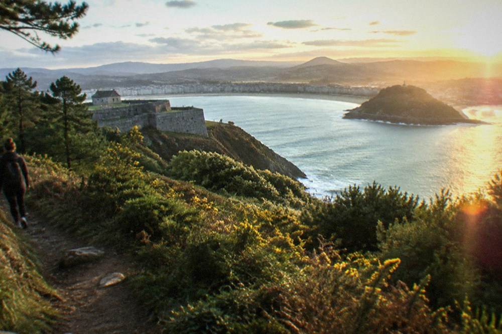 A hilltop path with an old stone fort and the curved bay below at golden hour