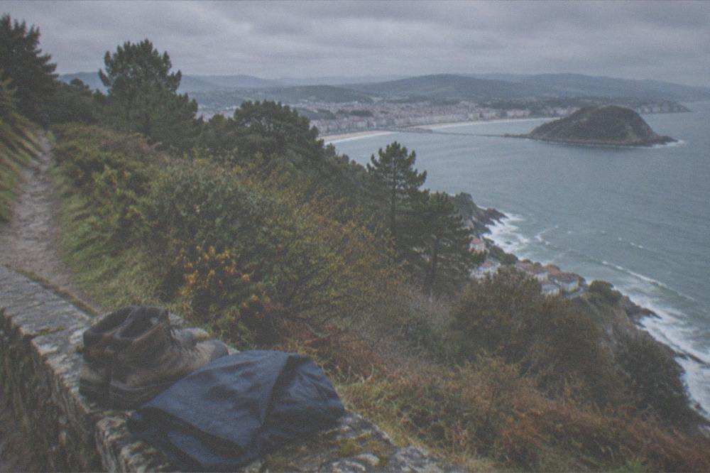 Walking boots and a folded rain jacket on a stone wall above a coastal town