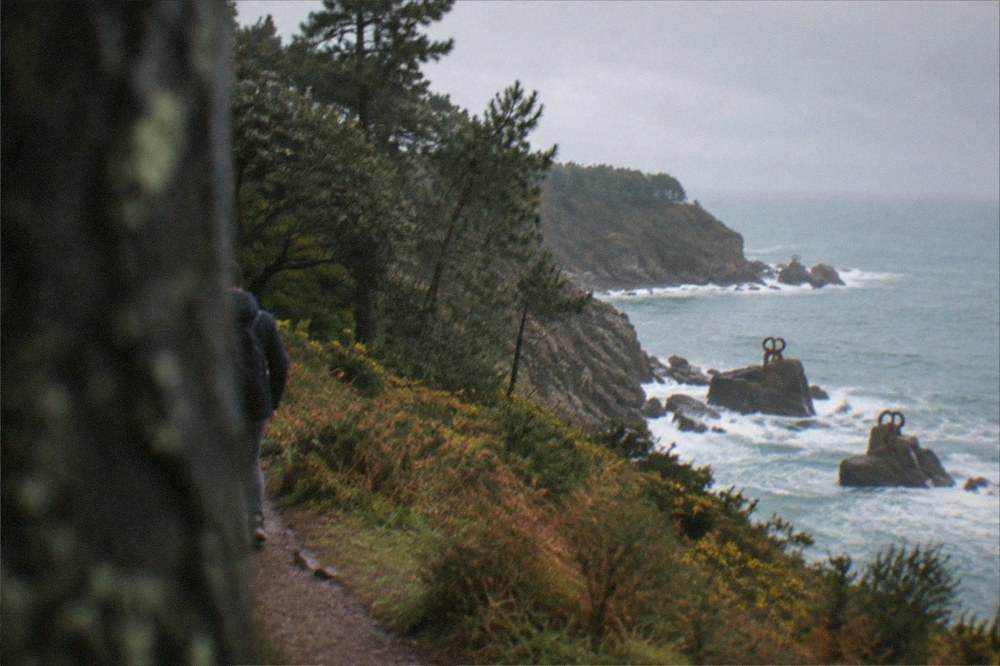 Steel sculptures on rocks at the water's edge with waves breaking around them