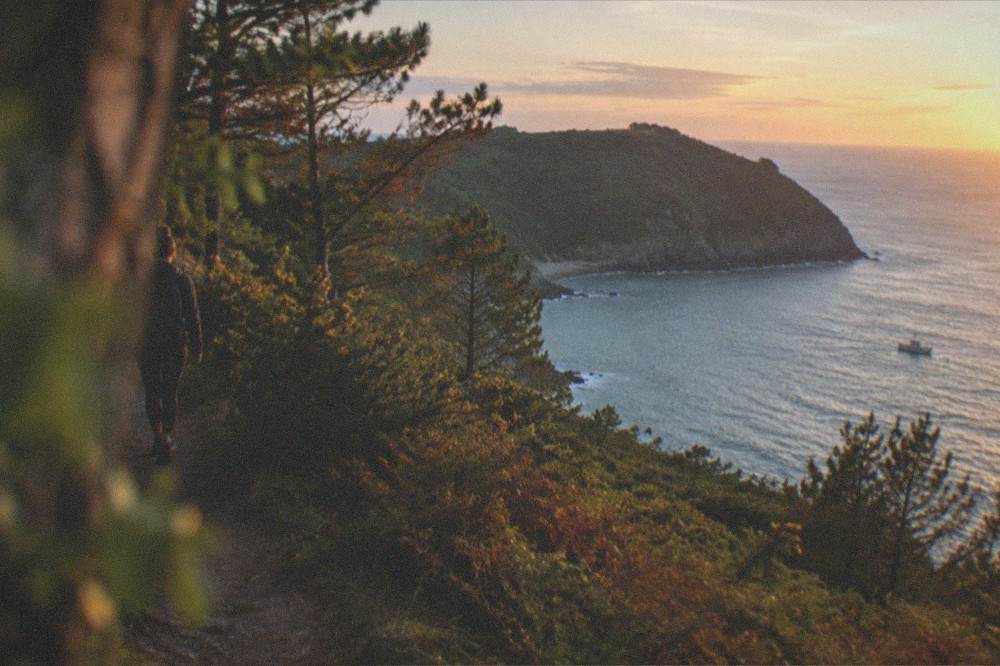 A green headland above the sea at sunset with a small boat in the bay