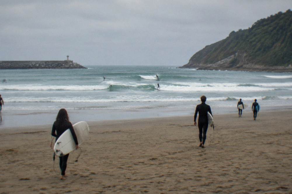 Surfers carrying boards across the sand at Zurriola beach in the Gros district