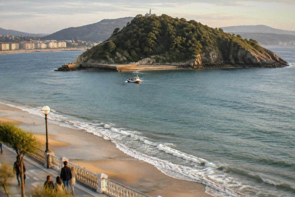 People walking the promenade beside La Concha beach with the bay and Santa Clara island behind