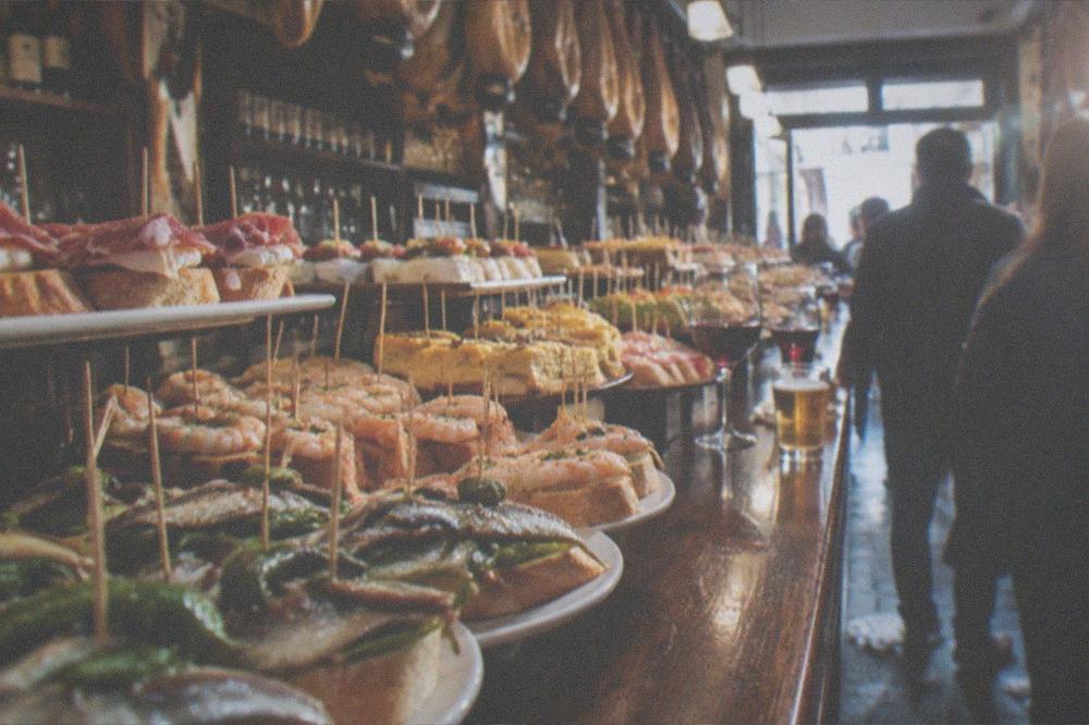 A pintxo bar counter loaded with small skewered bites and glasses of wine
