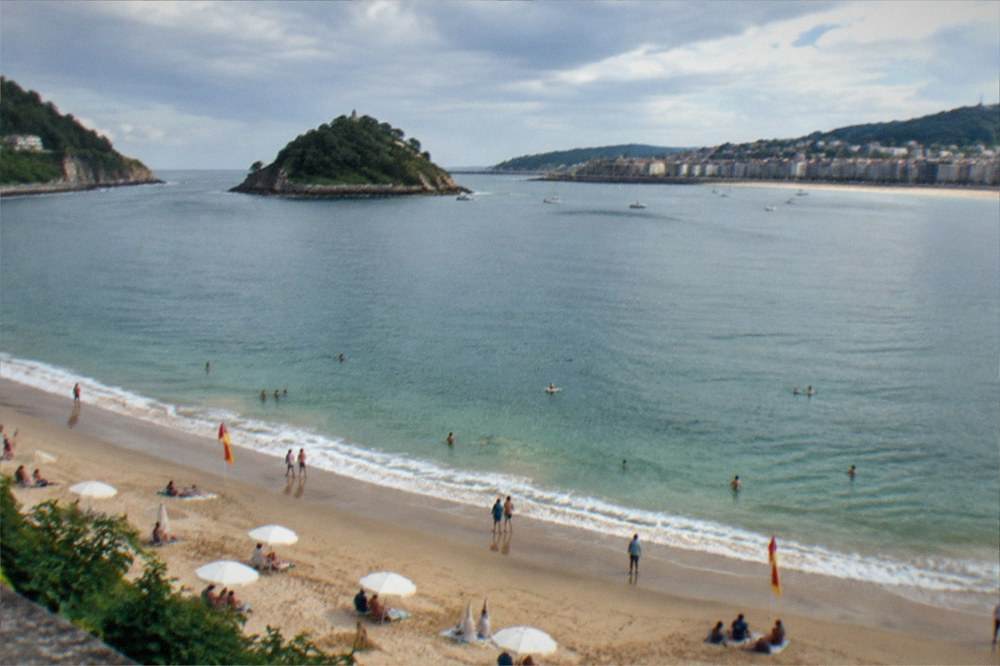 A swimming beach with lifeguard flags and parasols along La Concha bay in summer