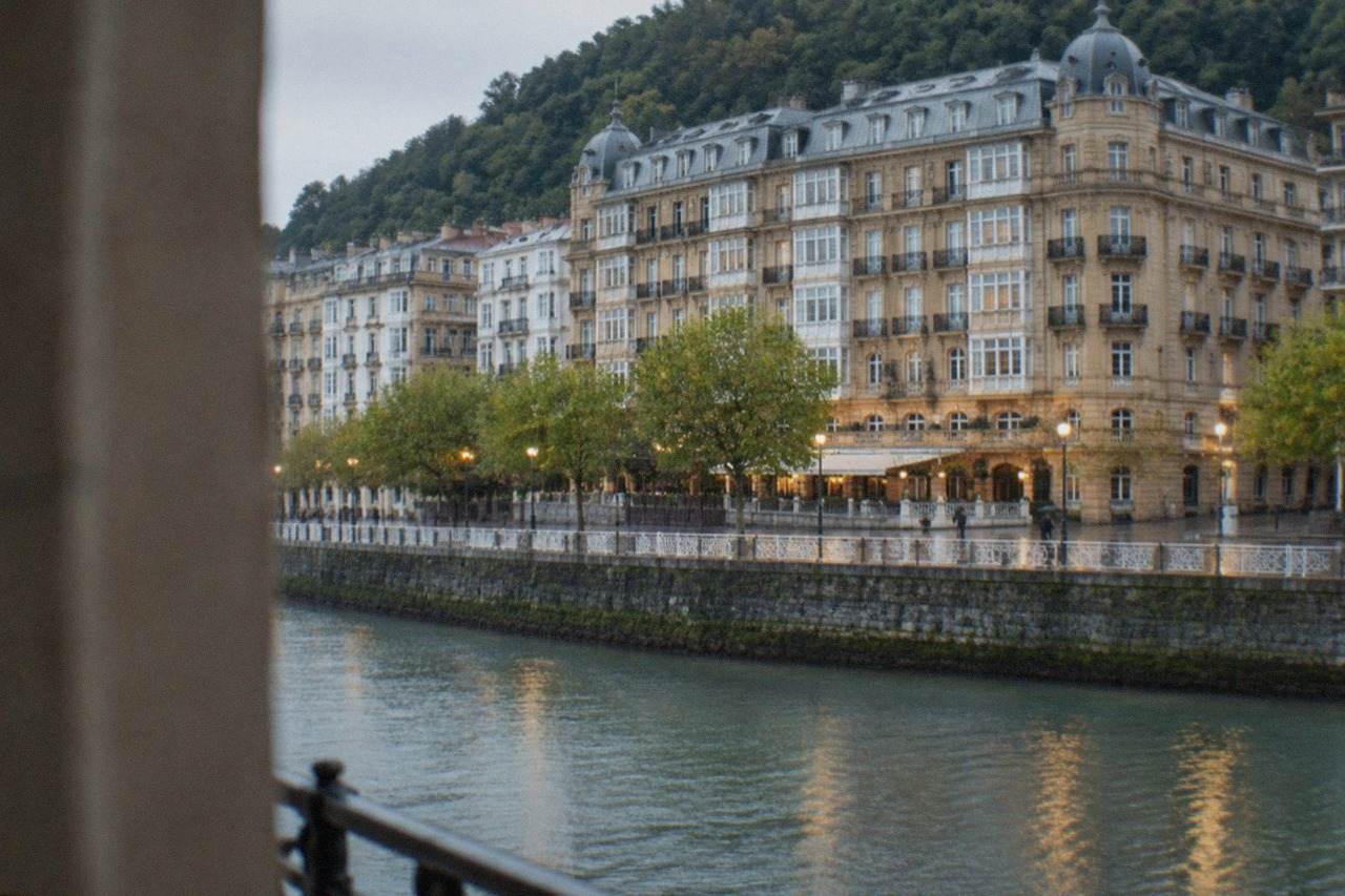 Grand historic hotel facade beside a river in San Sebastián at dusk