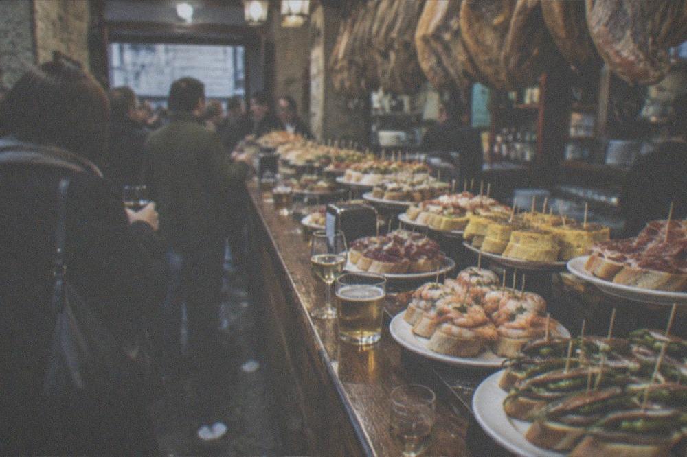 Crowded pintxo bar counter with small dishes and glasses of wine