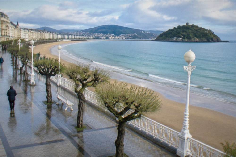 Curved sandy bay with an island and promenade in morning light