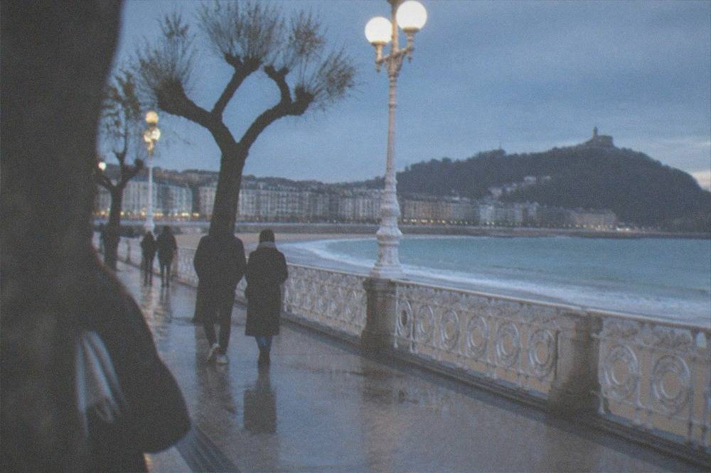 People walking the La Concha promenade with white railings and the bay beyond