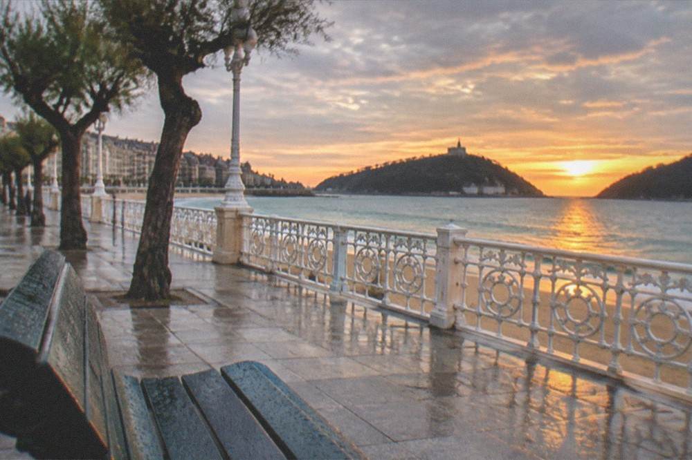 Sunset light over La Concha bay with the island and hills in silhouette from the promenade