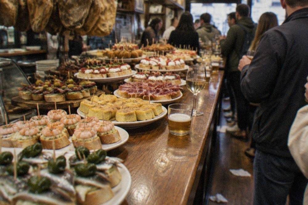 Crowded pintxo bar counter in the Old Town of San Sebastián with trays of small skewered servings