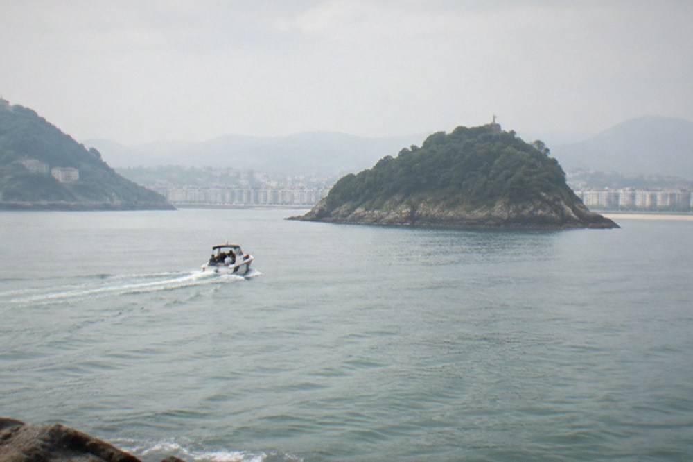 Small boat crossing La Concha bay toward Santa Clara island in San Sebastián