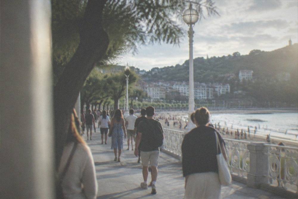 A busy seafront promenade in San Sebastián with a summer crowd walking between the balustrade and the beach