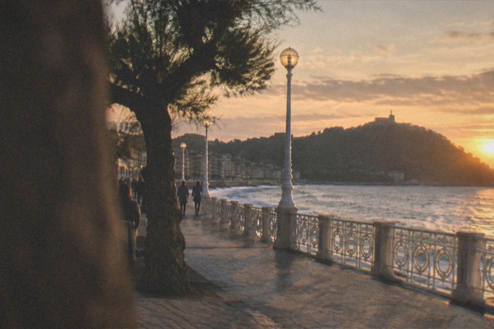 The seafront railing of La Concha promenade at dusk with street lamps lit and the silhouette of Monte Urgull beyond