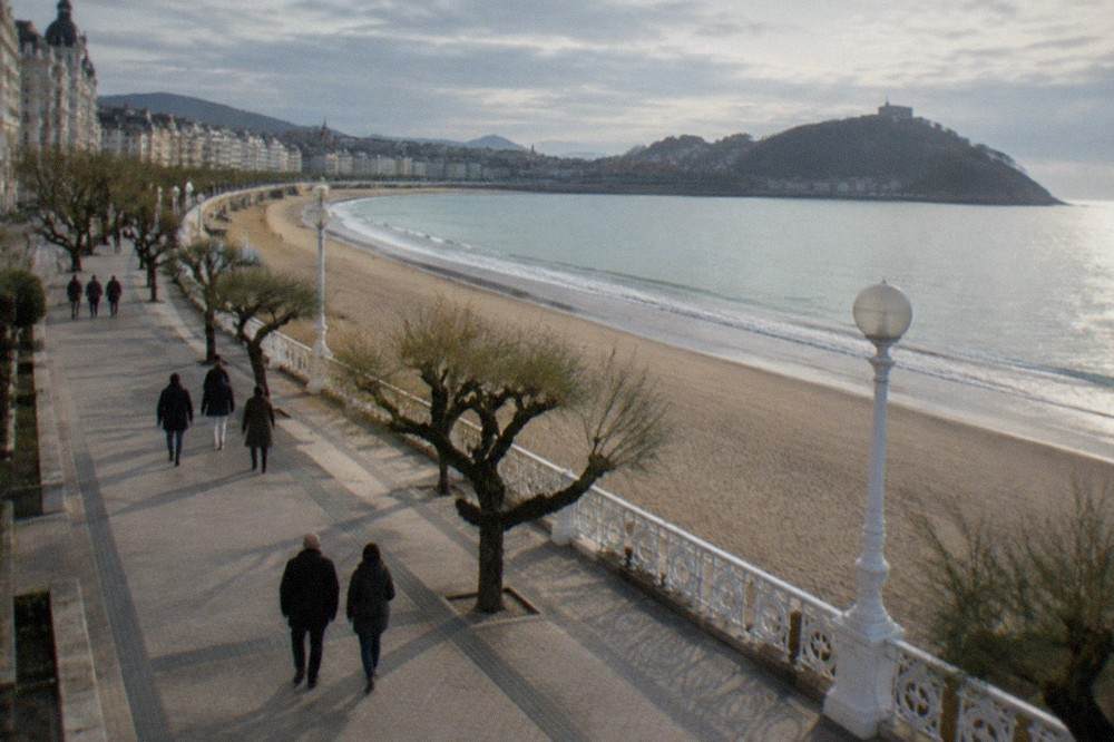People walking along the La Concha promenade with white railings, the beach on one side and grand buildings on the other