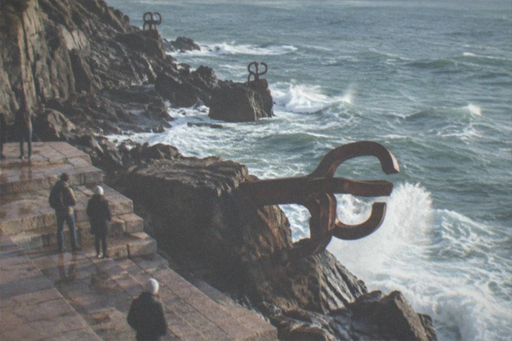 Waves breaking against the three steel sculptures of the Peine del Viento on the rocks at the end of Ondarreta beach