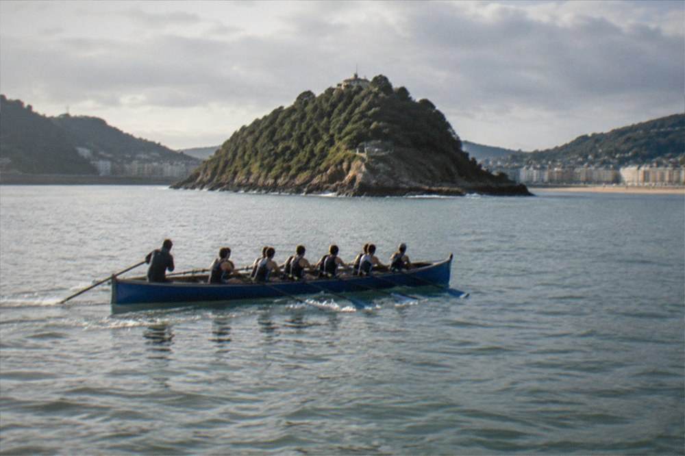 Rowers in a trainera boat pulling through the water in La Concha bay with the island behind