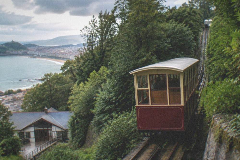 The white funicular cars on the Monte Igueldo rack railway climbing the wooded hillside above the city