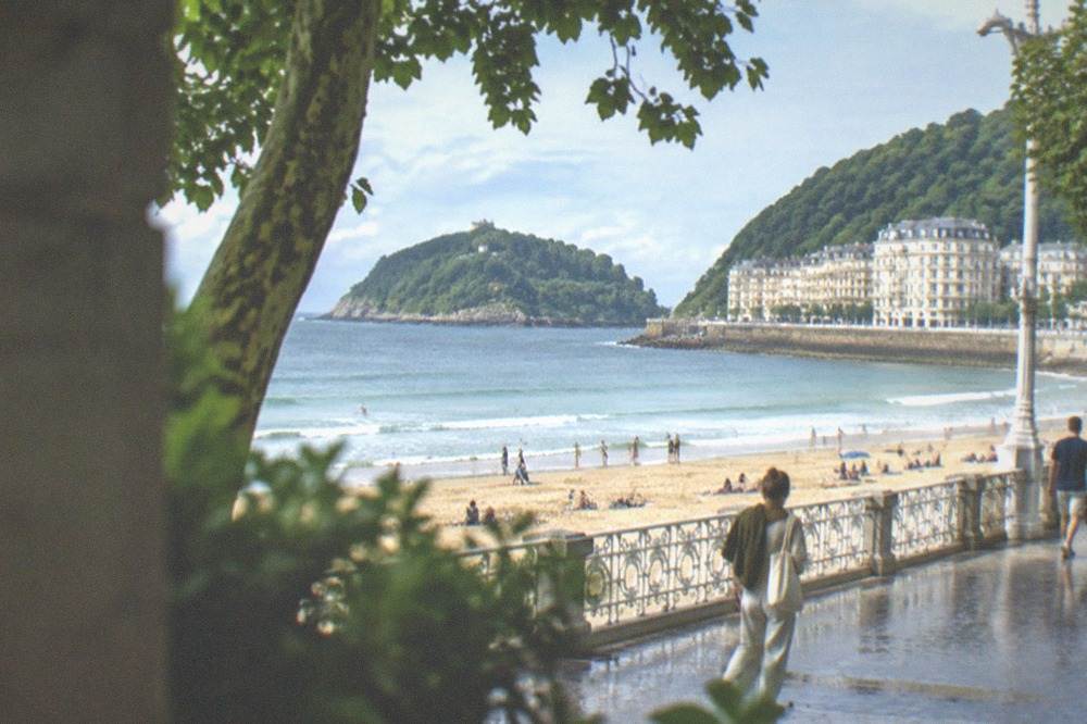 People on a sandy city beach with an island and hill behind