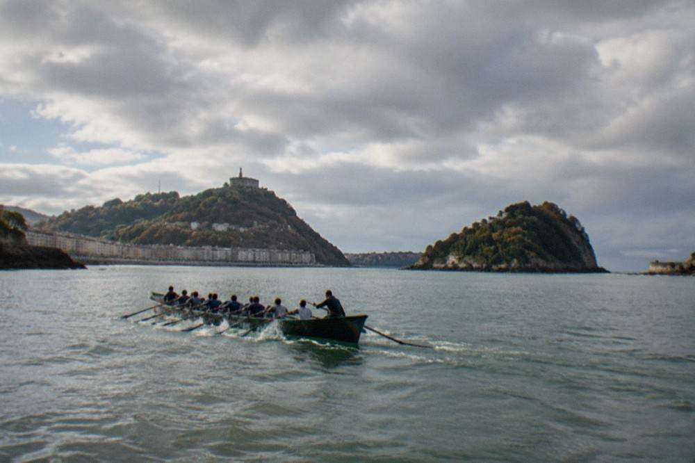 Rowers in a trainera pulling hard through the water with Monte Urgull behind them
