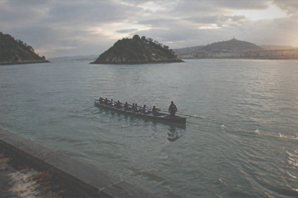 A trainera crew mid-stroke with all twelve oars in the water and the cox calling from the stern