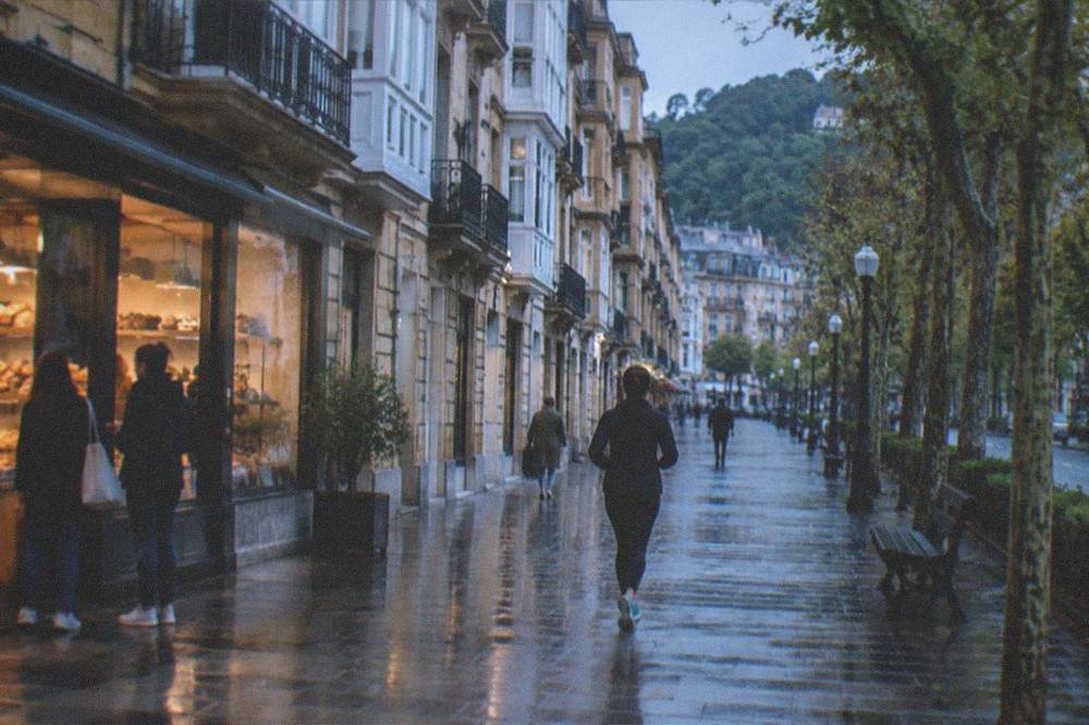 A morning street in San Sebastián with people greeting outside a bakery and bilingual signage visible