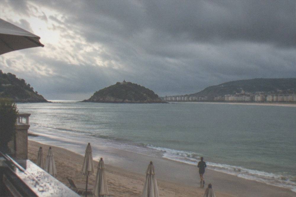 Rain clouds over La Concha bay seen from a hotel terrace with parasols on the sand