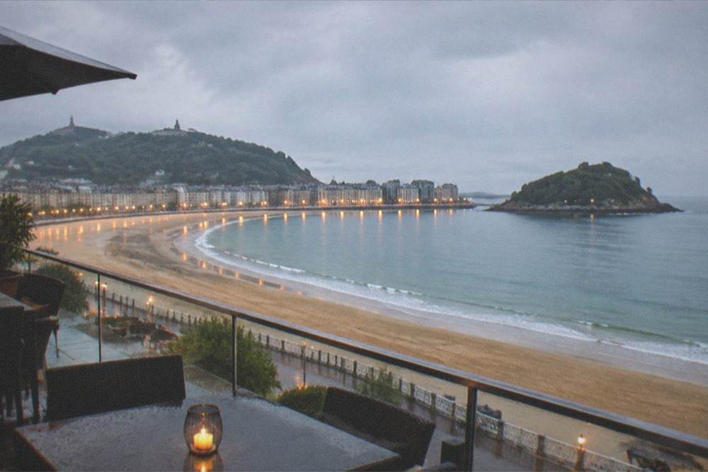 A hotel terrace at dusk with the illuminated curve of La Concha bay beyond