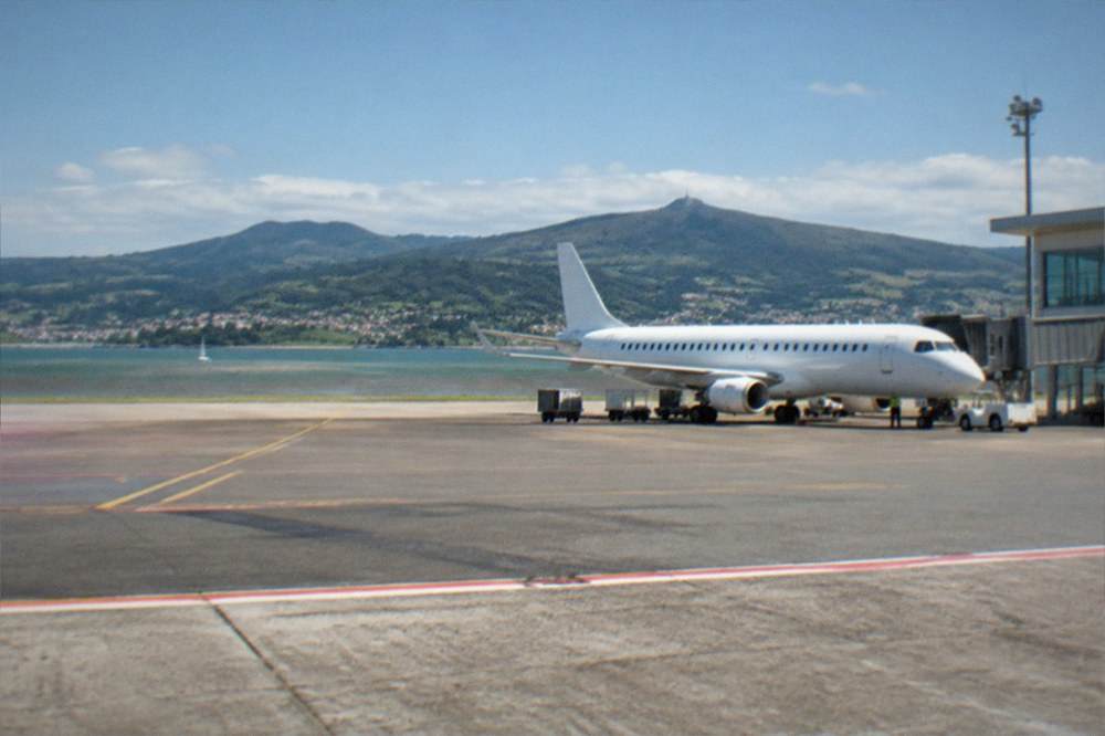Small regional airport terminal with a plane at the gate and hills beyond