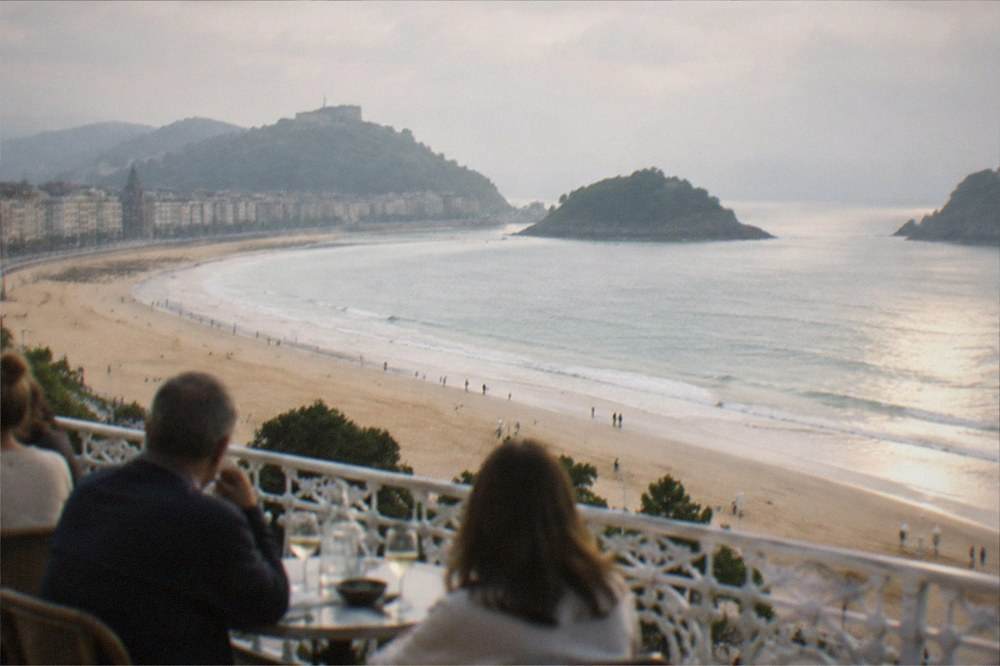 Diners at an outdoor terrace table above La Concha beach in warm evening light