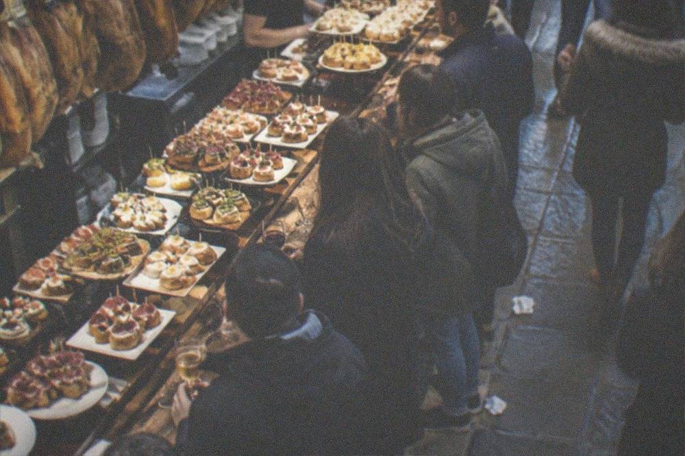 An evening street in an old town with lit pintxo bars and people walking