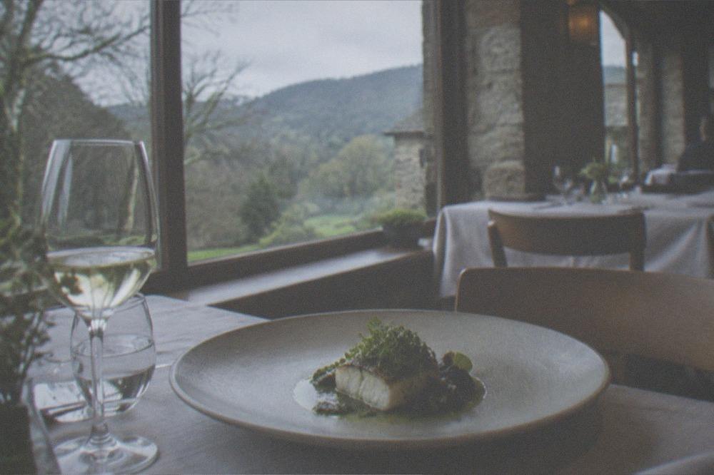 A dining room with linen-set tables and large windows onto countryside