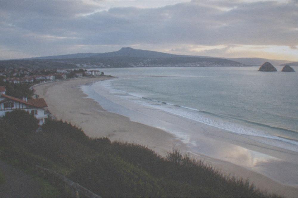 A hilltop viewpoint above a city with a curved bay and a long beach at dusk