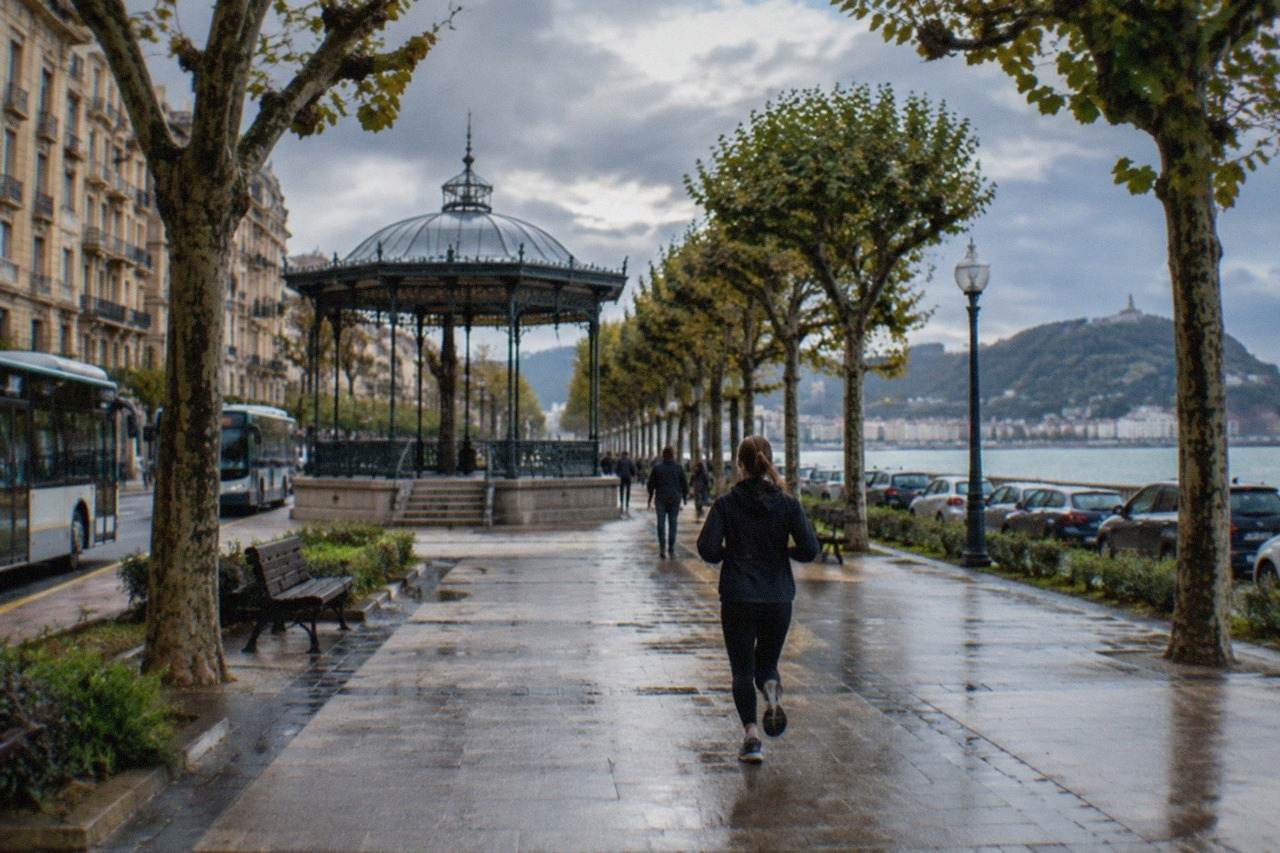 Cars parked along a tree-lined boulevard near the bay in San Sebastián with hills in the background