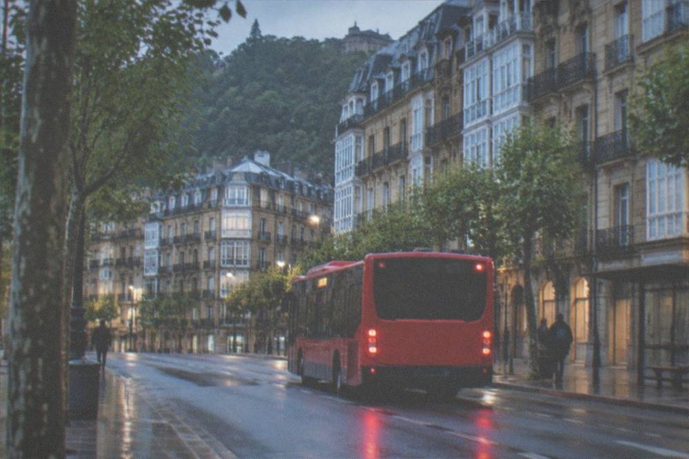A red city bus pulling away from a stop on a street in San Sebastián