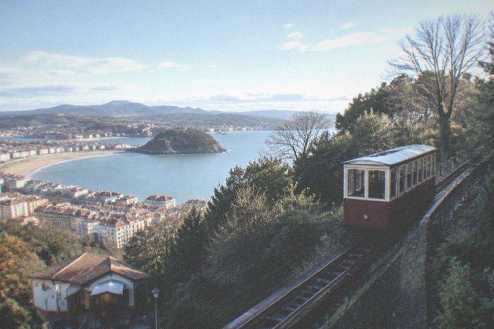 A funicular car climbing a wooded hill above rooftops and a bay
