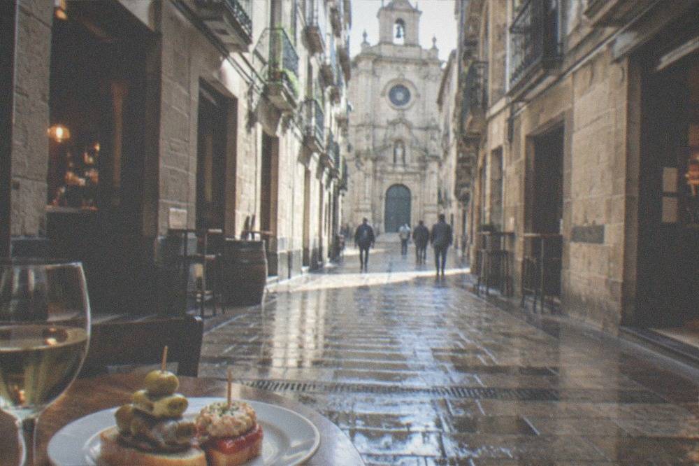 A plate of pintxos including an anchovy and olive skewer beside a small glass of white wine