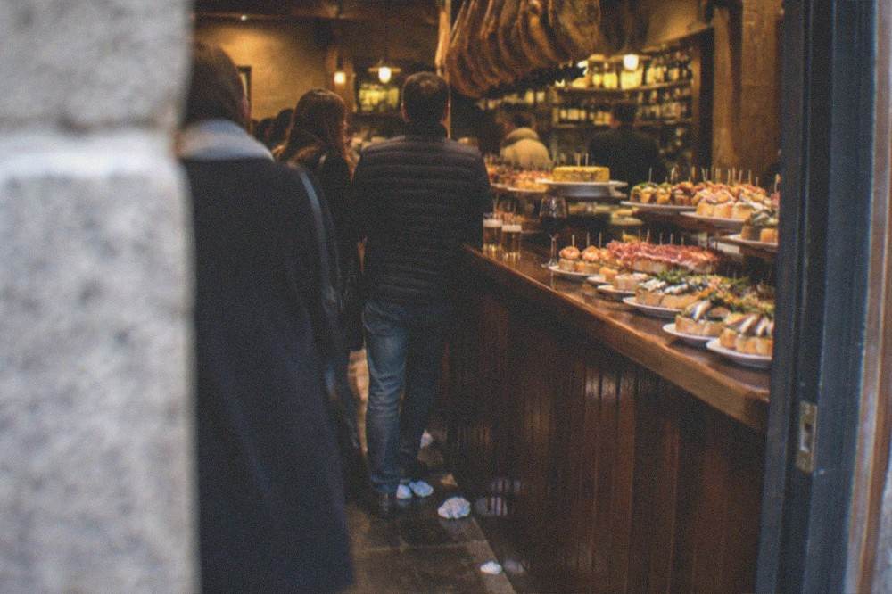 Evening view of a pintxo bar entrance in San Sebastián with warm light and people at the counter inside