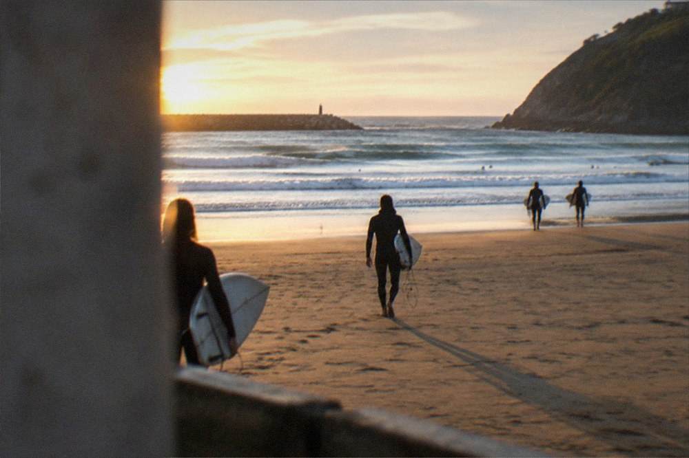 Surfers carrying boards across the sand at Zurriola beach at sunset