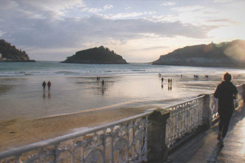People walking on the wet sand at low tide at La Concha with the island in the distance
