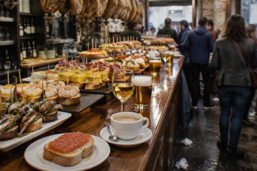 A toasted bread slice with tomato and olive oil on a small plate beside a coffee cup on a bar counter