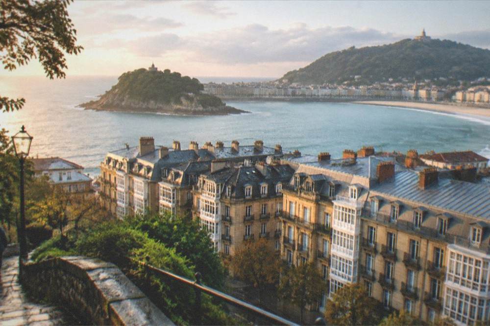 A view over the rooftops and bay of San Sebastián in early morning light from a hill path