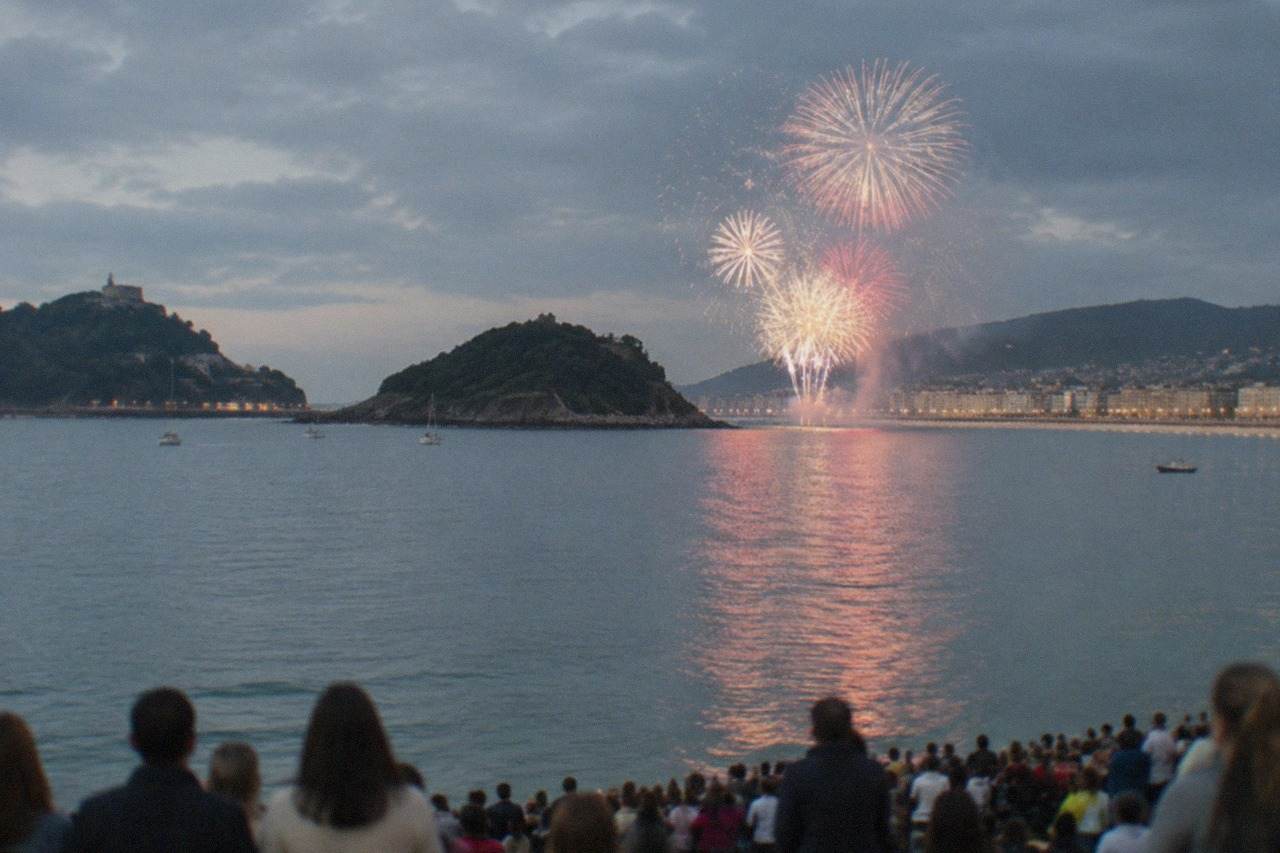 Crowds gathered along La Concha bay in San Sebastián at dusk with fireworks bursting over the water