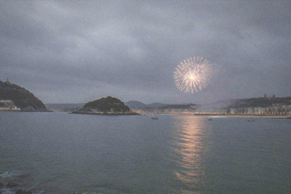 A fireworks shell bursting over La Concha bay seen from the city side at night